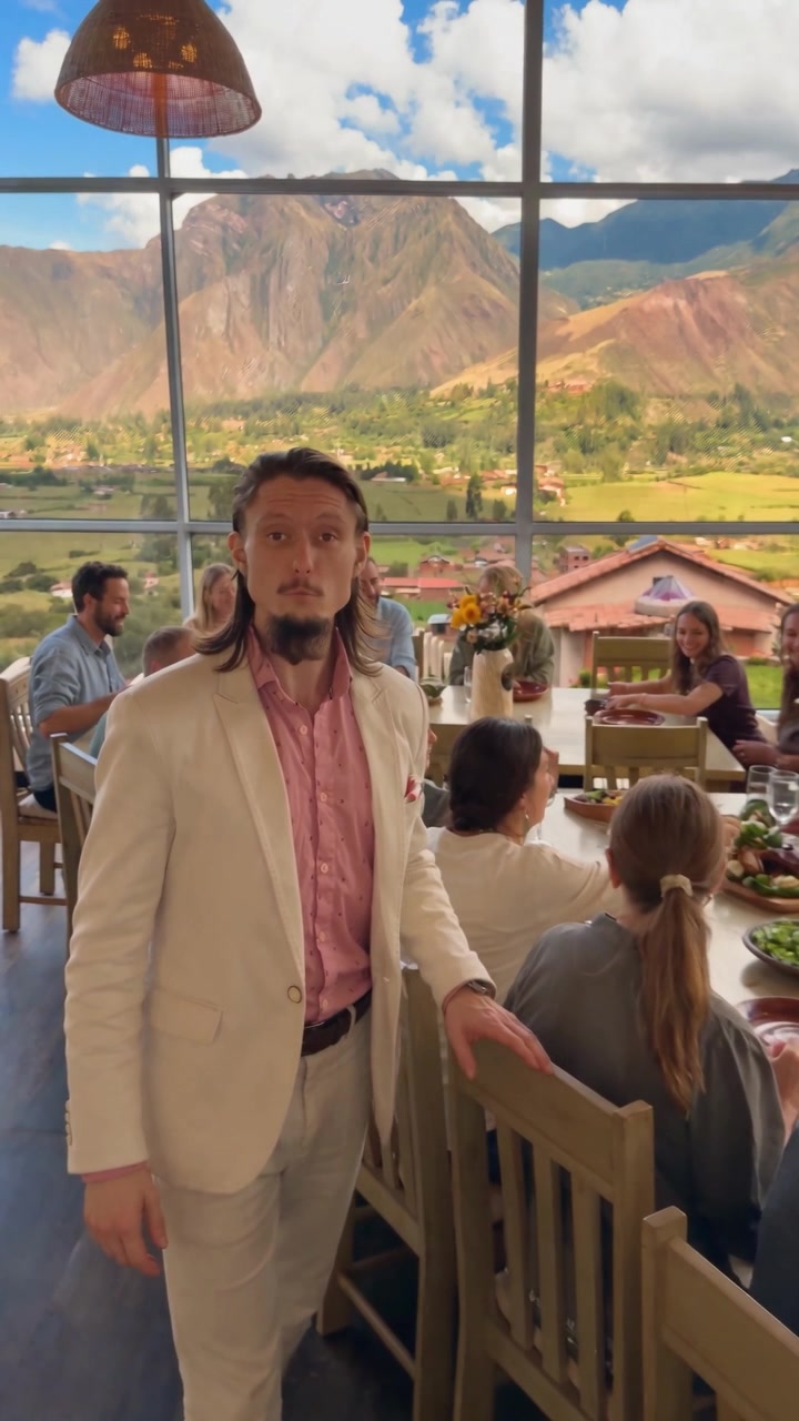 Florian Rolke in the glass dining room, a retreat group at the tables and the valley mountains behind